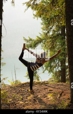 Fit woman performing stretching exercise in a lush green forest Stock Photo