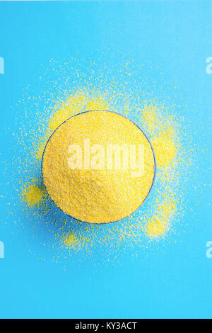 Bowl with Heap of Dry Uncooked Vibrant Yellow Color Polenta Spilled on Light Blue Background. Top View. Creative Image. Sun Imitation. Healthy Diet Me Stock Photo