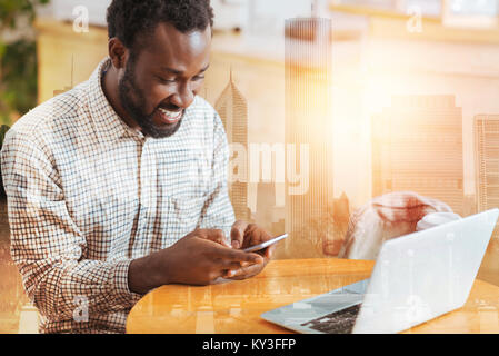 Cheerful dark-skinned man using his gadget Stock Photo
