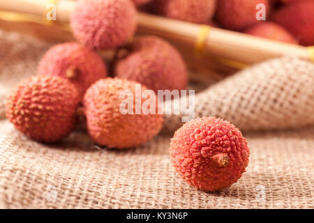 Studio shot with fruits (Lichi) of the lychee tree (Litchi chinensis) on coarse sackcloth fabric with a single sharply figured fruit in the foreground Stock Photo