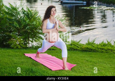 Pregnant woman in sports bra doing exercise in relaxation on yoga. Pose of the hero. Virabhadrasana. Stock Photo