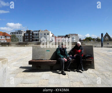 Couple sat on modern memorial bench on Portsmouth seafront, Old Portsmouth, Hampshire, England, UK