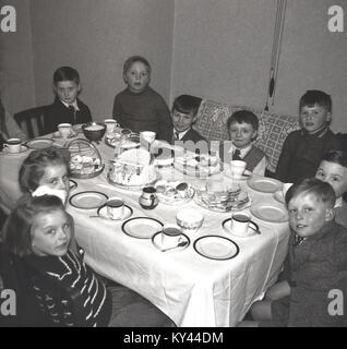 1950s Britain and no fizzy sugary drinks in sight!.....historical picture of a group of young children - many of the boys are wearing ties! - sitting together around a table with a tablecloth celebrating a birthday, with a cake, sandwiches and a cup of tea, England, UK. Stock Photo