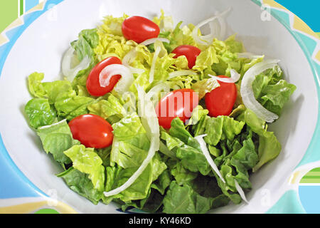 Fresh chopped Romaine lettuce, ripe cherry tomatoes and sliced white onion in a colorful salad bowl Stock Photo