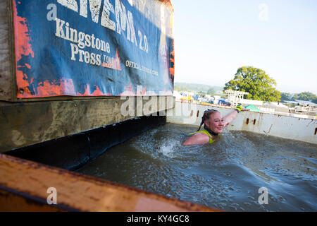 Sussex, UK. A young woman grimaces as she swims through a pool of ice water during a Tough Mudder obstacle course. Stock Photo
