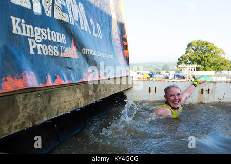 Sussex, UK. A young woman displays a pained smile as she swims through a pool of ice cold water during a Tough Mudder obstacle course. Stock Photo