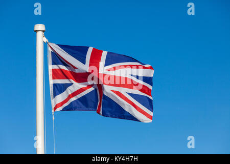 Union Jack flag and flagpole on a bright blue sky background blowing in the wind