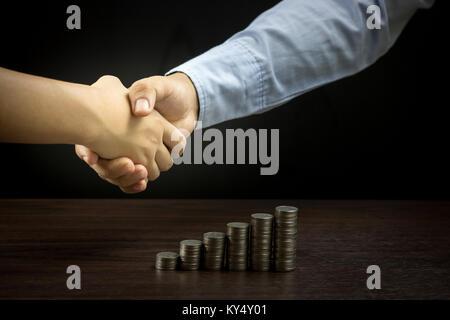 businessman shake hand with stacked of  coin on wood table, concept as cooperate and teamwork to success in business Stock Photo