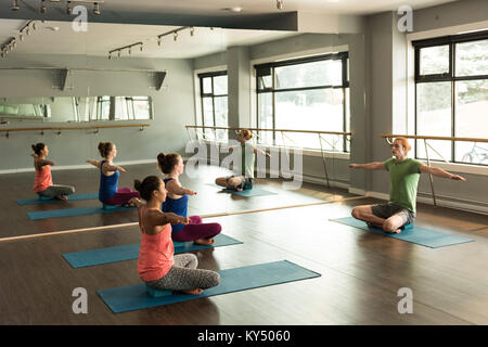 Trainer assisting women in practicing yoga Stock Photo