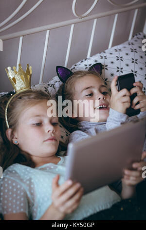 Siblings using mobile phone and digital tablet on bed Stock Photo