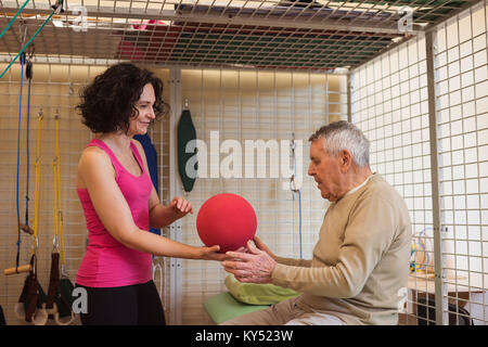 Female therapist assisting senior man with exercise ball Stock Photo