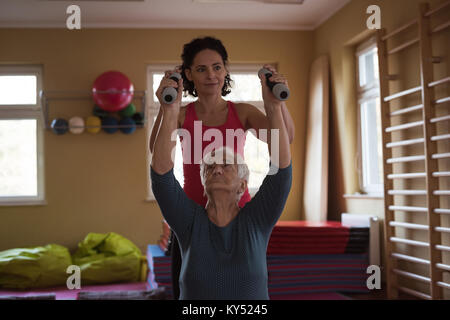 Female therapist assisting senior woman with dumbbells