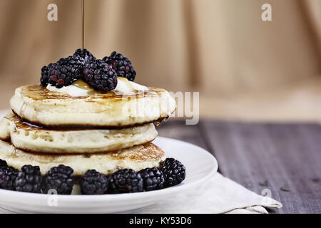 Stack of homemade pancakes with blackberries, melting butter and syrup being poured onto them. Extreme shallow depth of field. Perfect for Shrove Tues Stock Photo