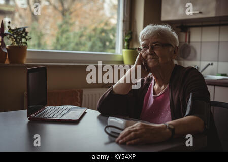 Senior woman sitting with blood pressure machine and a laptop Stock Photo