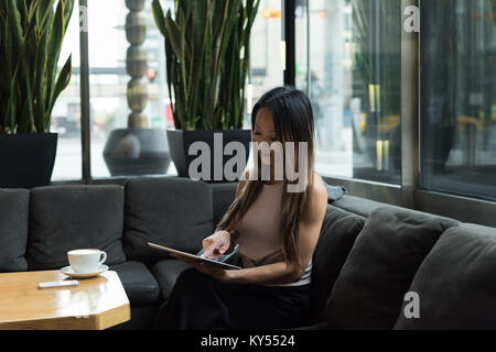 Businesswoman sitting on sofa working on her tablet Stock Photo