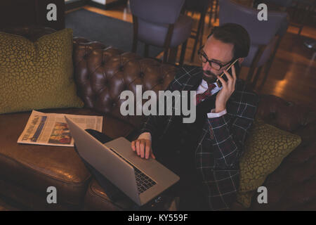 Businessman taking on mobile phone while using laptop Stock Photo
