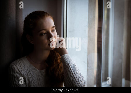 Thoughtful woman looking through window Stock Photo