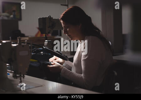 Tailor looking through magnifying glass while stitching a clothes Stock Photo