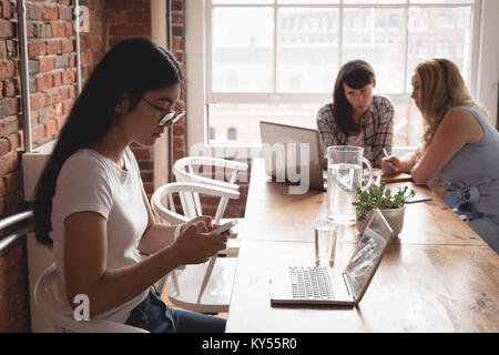 Executive using mobile phone while colleagues discussing in background Stock Photo