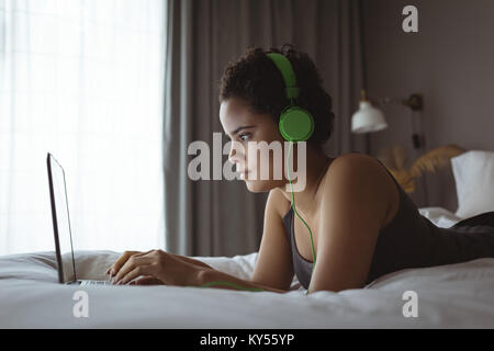 Woman using laptop while listening to music on bed Stock Photo