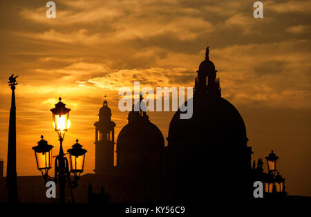 Venice sunset with Salute Basilica (Saint Mary of Health) baroque domes, lamp and Saint Mark Lion silhouette Stock Photo