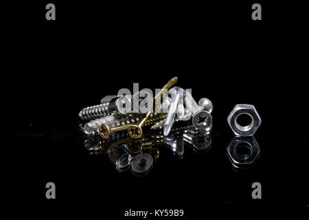 Screws and screws with reflection in the mirror. Screws on the glass mirror table. Black background. Stock Photo