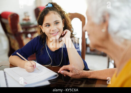 Happy little girl doing school homework with elderly woman at home. Family relationship with grandmother and granddaughter. Grandma teaching, female g