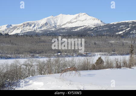 Two skeleton sweat lodges sit in a snow covered field with a magnificent mountain and lake background view Stock Photo
