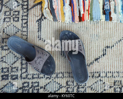 Old gray slippers on the doorstep of a house on a homespun carpet, top view. Stock Photo