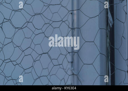 Up close, isolated shot of chicken wire, with a white wall and a chrome bar in the background, in black and white Stock Photo