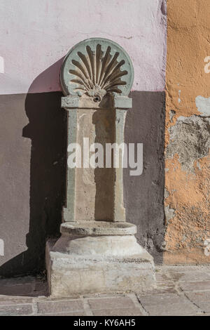 Isolated shot of an old stone water basin on a stone pedestal, with aged colorful stone walls and a stone walkway, in Guanajuato, Mexico Stock Photo