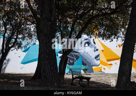 Corsica: a bench under the shadow of a tree in a public area of Furiani, little town of the Haute Corse, with a big murales on a wall Stock Photo