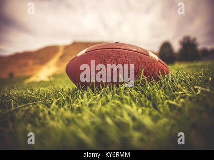 a brown american football lying on green grass in a field with a hill and trees in the background toned with a retro vintage instagram filter app or a Stock Photo