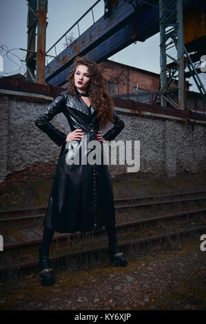 Fashion shot: portrait of a beautiful goth girl (informal model) in leather coat standing at railroad (industrial area) Stock Photo