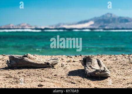 Pair of old shabby shoes on the sandy beach. Old shabby shoes on the sand. Stock Photo