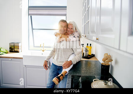 Affectionate senior couple smiling and sharing a romantic moment together while relaxing in their kitchen at home Stock Photo