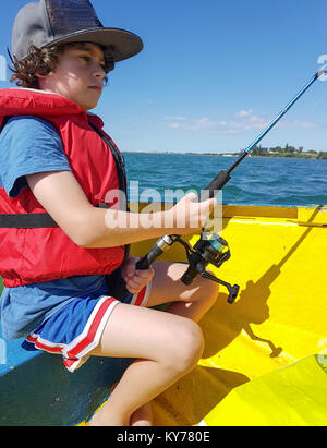 Smart phone image kid fishing from small dinghy on Tauranga Harbour in bright yellow dinghy. Stock Photo