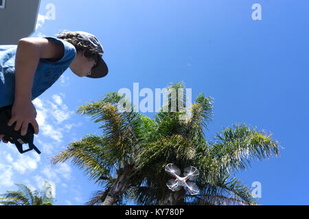 Boy flying small drone amongst trees under blue sky low angle point of view Stock Photo