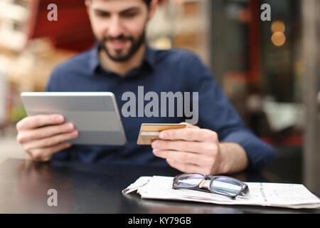 Gladden prosperous man purchasing at online shop with money card and tablet with close up face in  . Satisfied man sitting at street cafe and smiling. Stock Photo