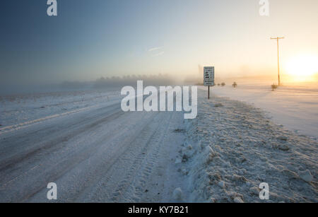 Winter Driving Background. Rural country snow covered road with a frigid winter wind blowing snow across the horizon. Stock Photo