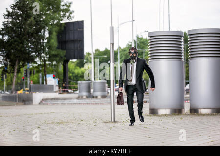 Businessman running with briefcase wearing a gas mask Stock Photo