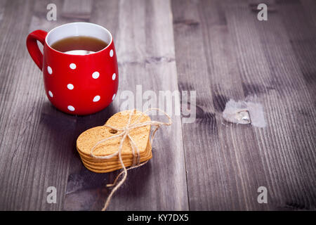 Red cup in a white point is on a white wooden table. Paper hearts hang on the wall Stock Photo