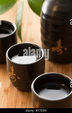 Japanese Sake rice wine in black and gold cups with sake bottle on a bamboo background Stock Photo