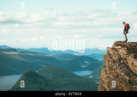 Man explorer standing on cliff alone mountain summit over fjord Norway landscape Travel Lifestyle success motivation concept adventure active vacation Stock Photo