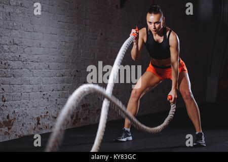 Battle ropes session. Attractive young fit and sportsman working out in ...