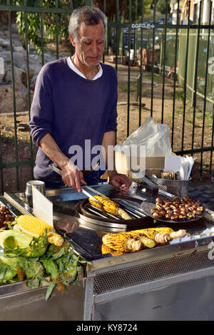 Street vendor cooking and selling roasted corn on the cob and conkers (chestnuts),  Apostolou Pavlou pedestrianized street, Athens, Stock Photo