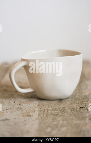 handmade, uneven, quirky white ceramic cup on a raw wooden plank Stock Photo