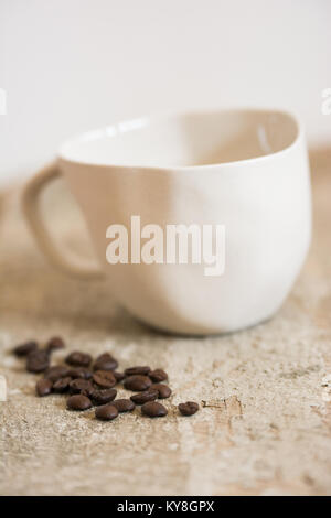 handmade, quirky white cup with coffeebeans spilled next to it Stock Photo