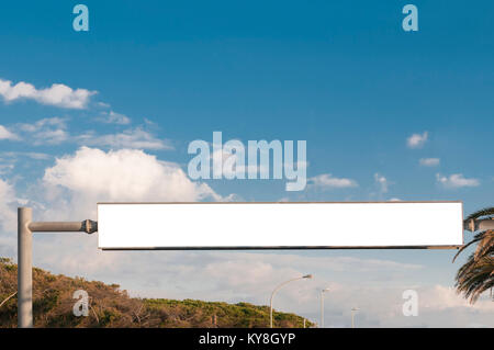 Large rectangular blank billboard crossing the street with sky and trees on backgroun Stock Photo