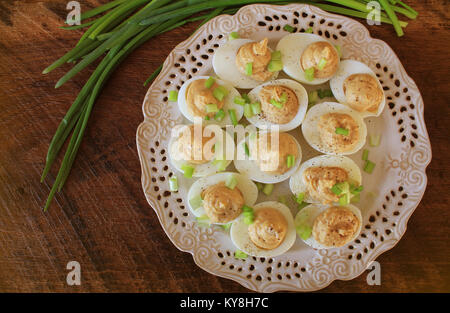 Deviled eggs with cod livers with leek on white plate. Rustic wooden table Stock Photo